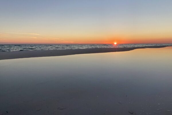 A serene photo of a sunset, with the sun just touching the horizon, on the Gulf of Mexico