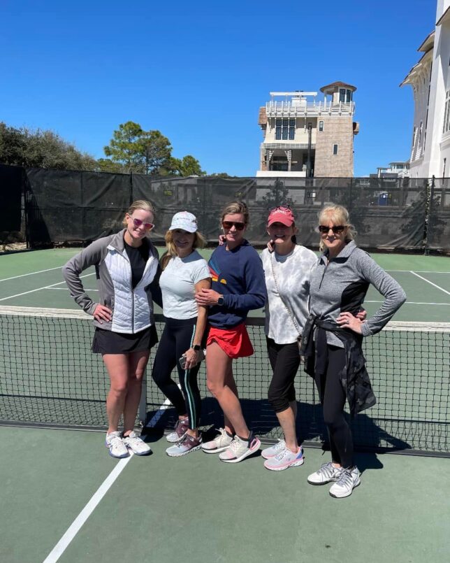 Five female Watersound Club members pose together on the Watersound Beach Club tennis court after a pleasant match on a beautiful afternoon