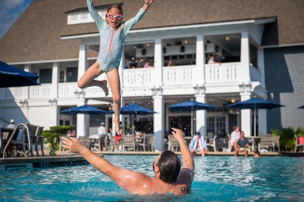 Watersound Club members, a father and daughter, laughing and having fun in the Watersound Beach Club pool as the dad launches the little girl into the air, prepared to make a big splash!