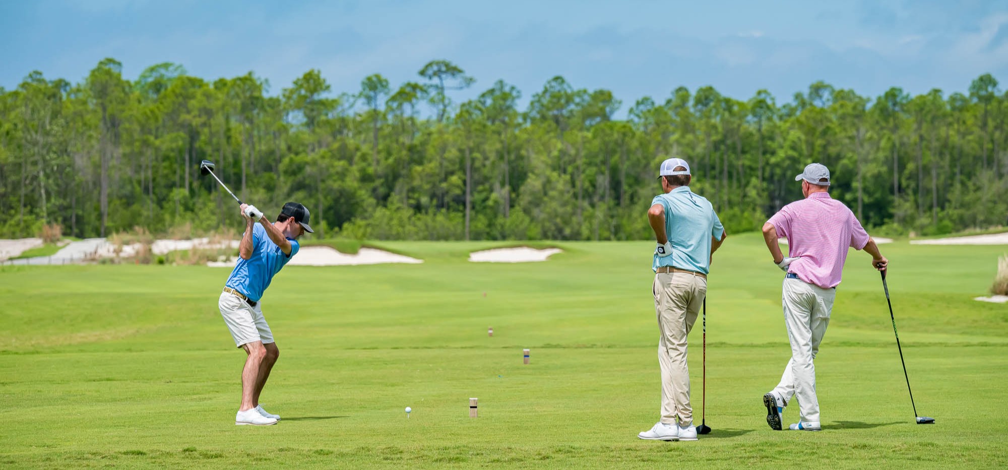 A golfer tees off on The Third golf course in Panama City Beach, Florida, while two golfers look on down the fairway.